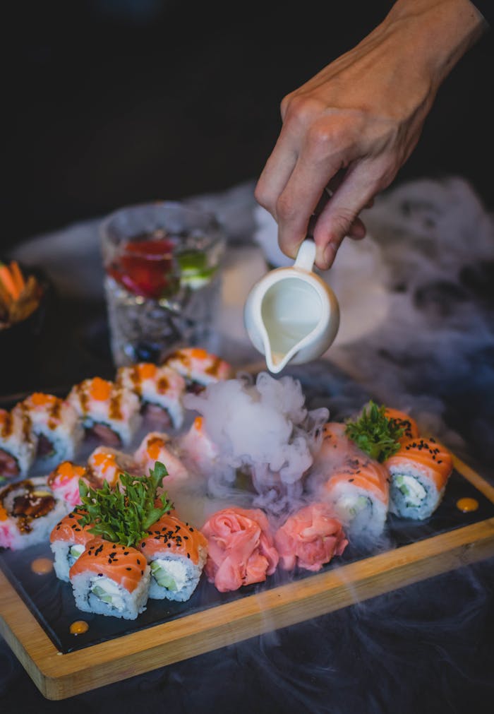 services-02 A hand pouring sauce over sushi rolls with a captivating smoke effect.