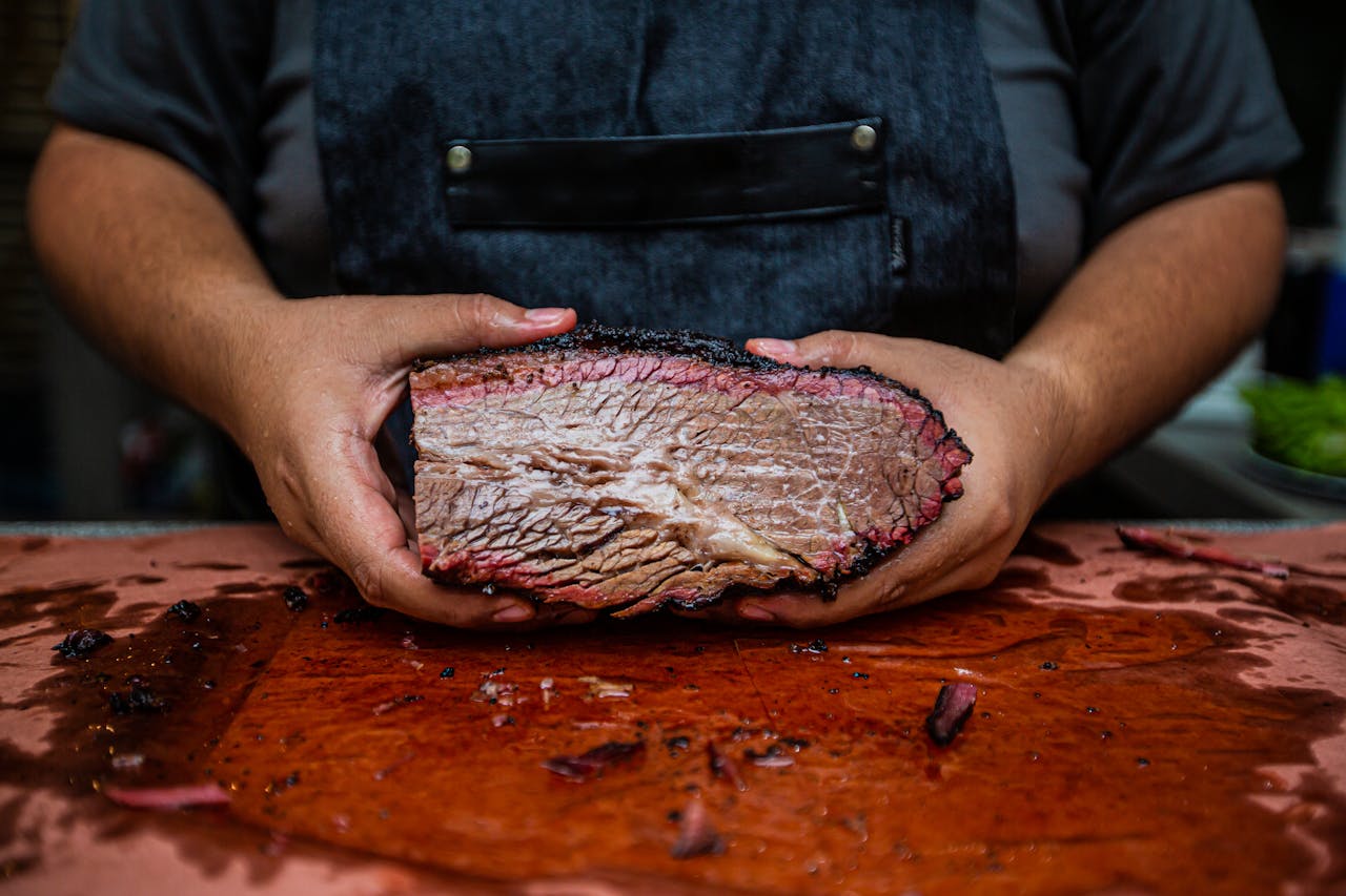 gallery-02 Close-up of hands holding a juicy smoked beef brisket on a wooden cutting board, showcasing rich texture.