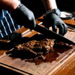 Chef slicing a juicy steak on a wooden board in a restaurant kitchen.
