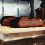 Close-up of two slices of smoked brisket on a kitchen cutting board, showcasing a perfect barbecue finish.