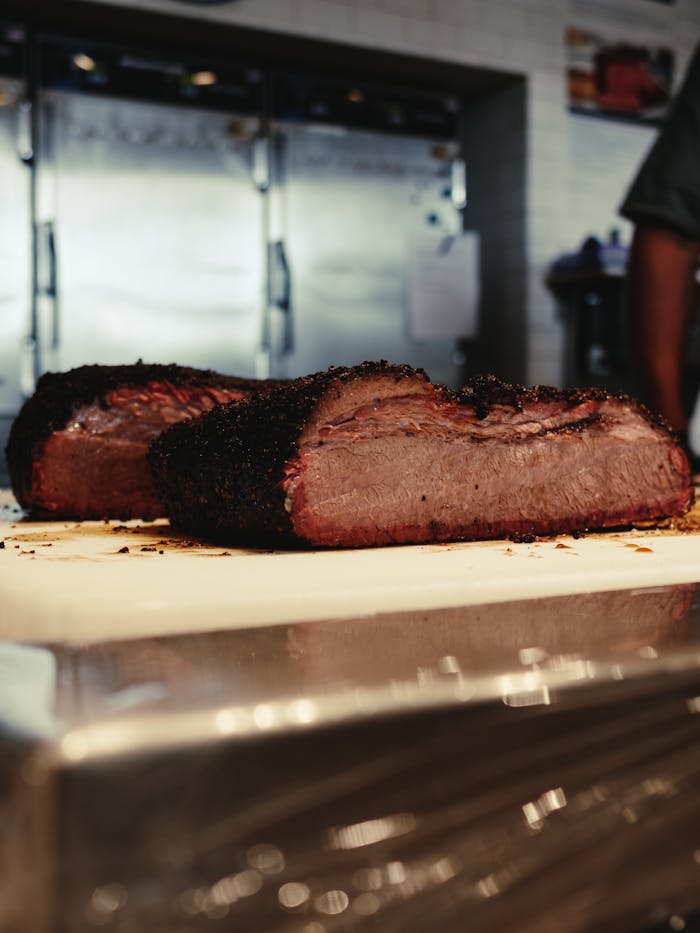 gallery-04 Close-up of two slices of smoked brisket on a kitchen cutting board, showcasing a perfect barbecue finish.