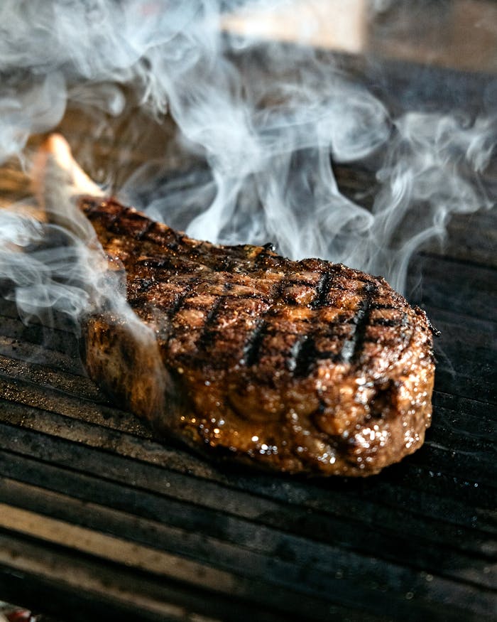 services-03 Mouthwatering steak with smoke rising, grilled to perfection on a barbecue grill.